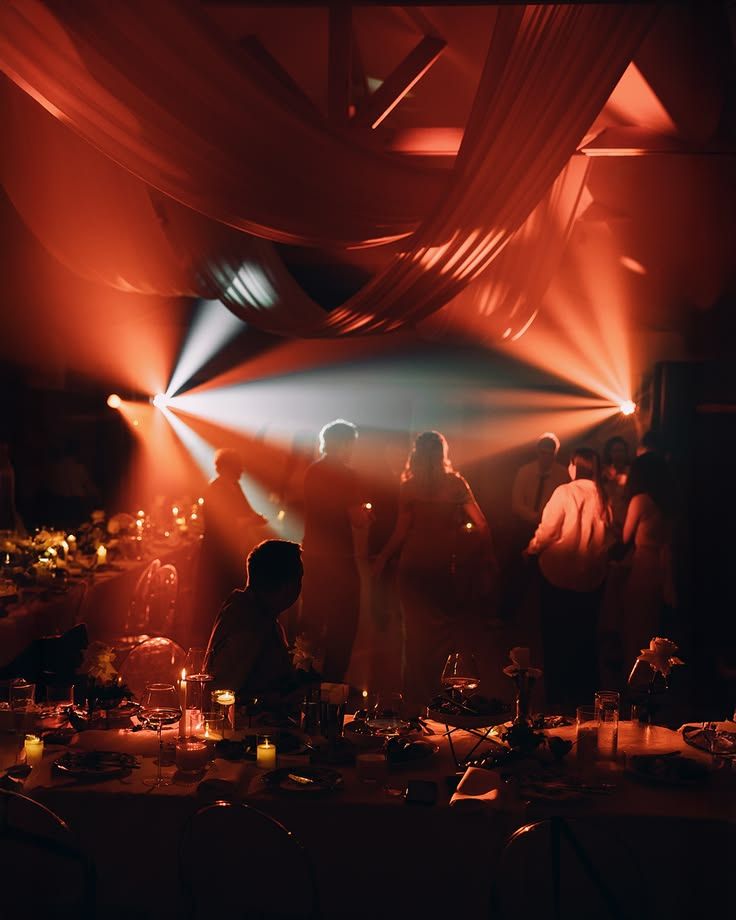 Wedding reception dance floor lit by warm beams under draped ceiling fabric